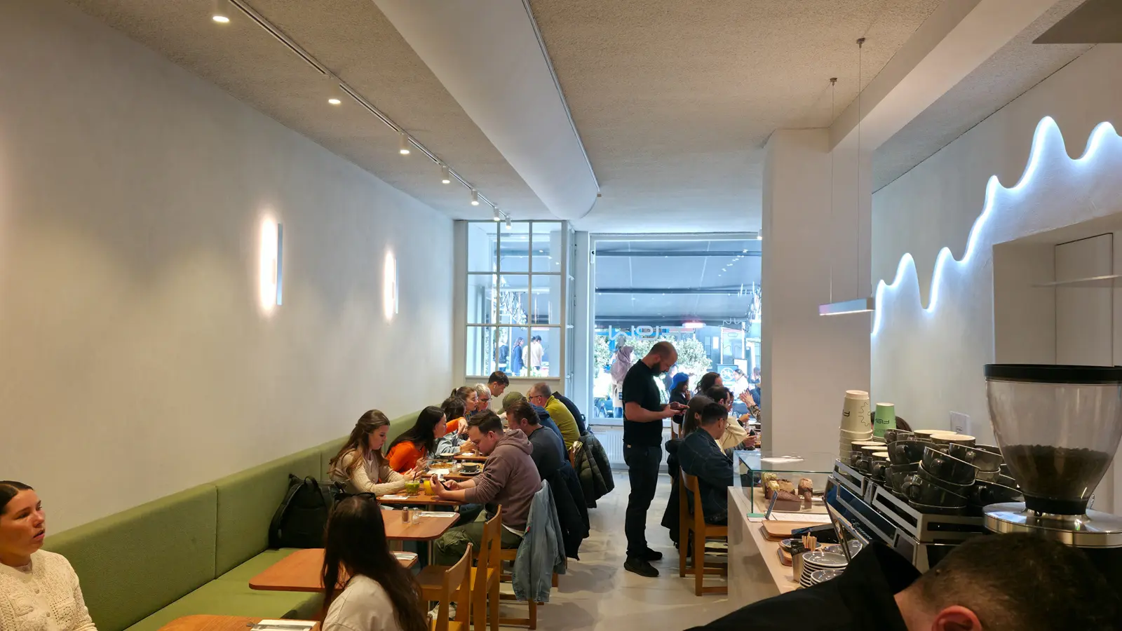 The long narrow room at Flow, with a sage green banquette down one side, wooden tables, and a wave of neon light above the counter