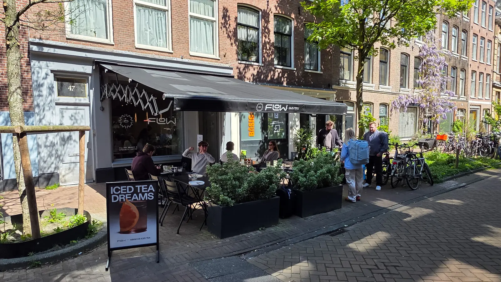 Flow seen along the street in Amsterdam, its number 47 door on the left, terrace tables under the awning and wisteria in flower beyond