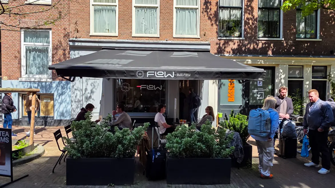 The grey awning and terrace at Flow in Amsterdam, with people at outdoor tables under trees and the logo across the canopy