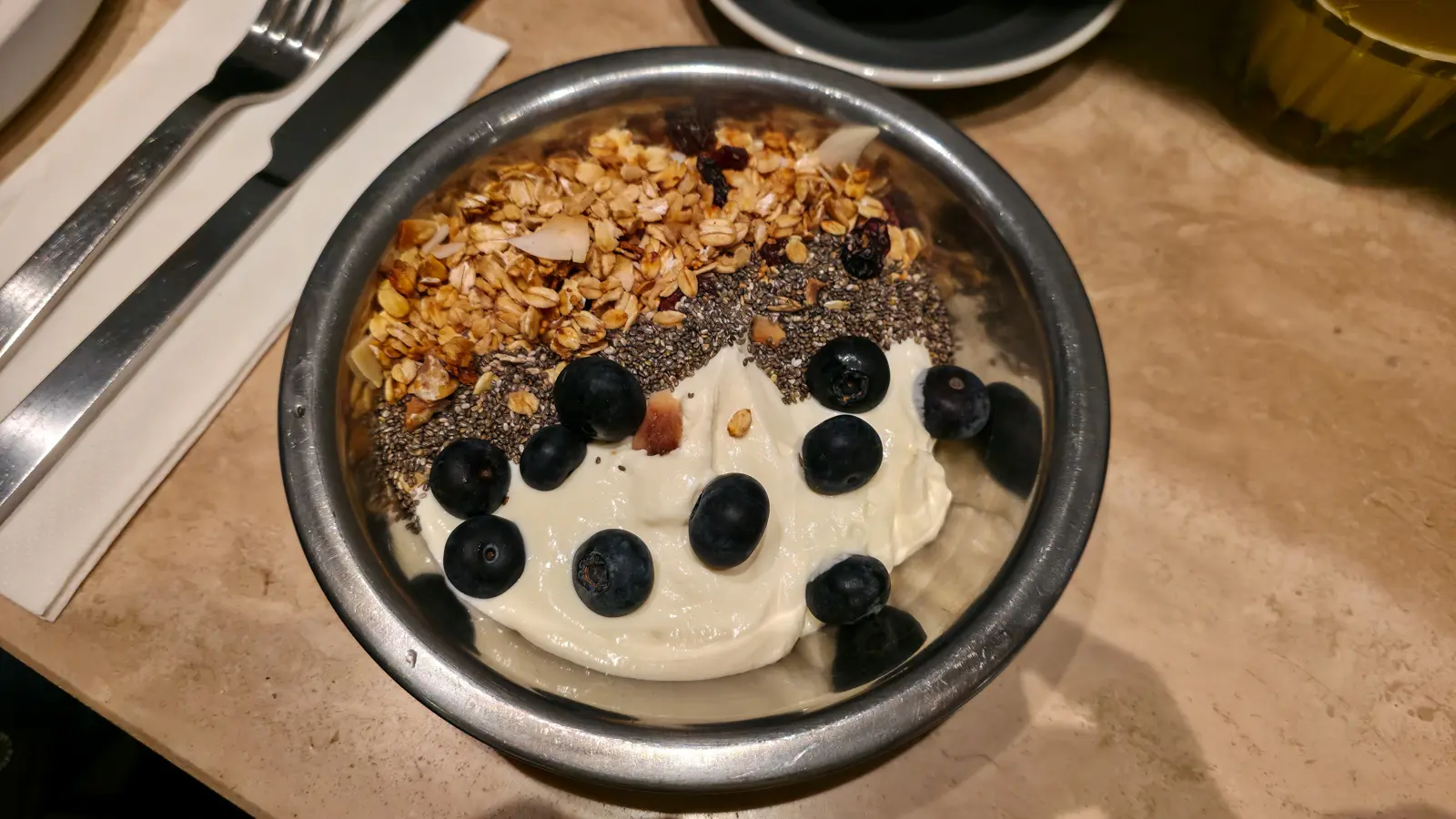 Whipped yoghurt at Flow in a steel bowl, with blueberries on the yoghurt, a band of chia seeds and a band of granola alongside