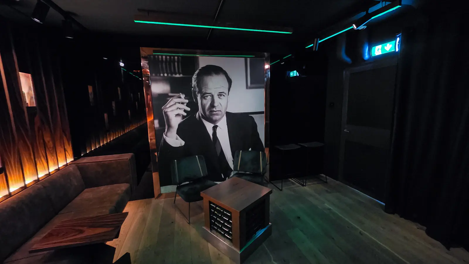 A large black-and-white portrait of Freddy Heineken smoking, mounted above a banquette and low chairs at the end of Freddy’s bar