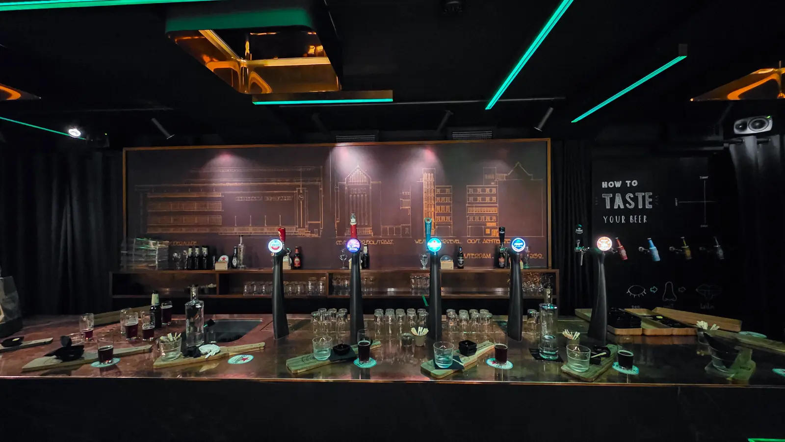 Five illuminated tap towers along the copper bar at Freddy’s, with lit architectural drawings behind and a tasting board to the right