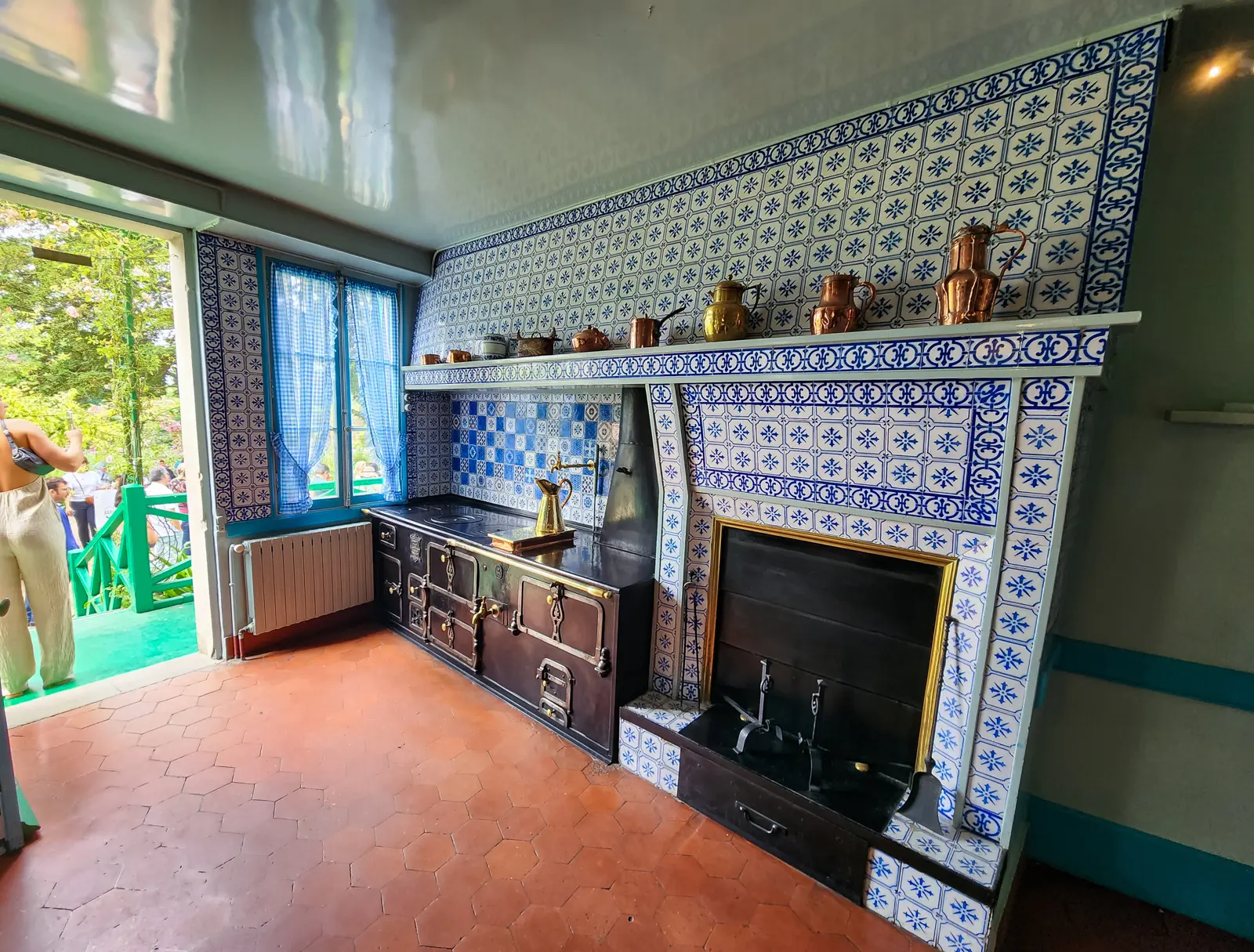 Monet’s kitchen at Giverny, tiled floor to ceiling in blue and white, with copper and brass pans on the mantel and a black range