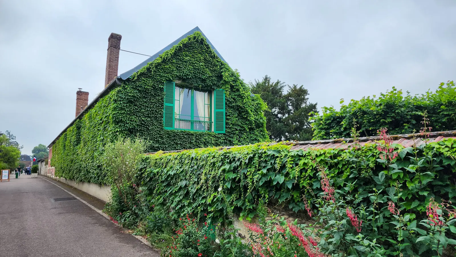 Monet’s house at Giverny from the street, its gable covered in ivy, green shutters at the window and creeper spilling over the wall below