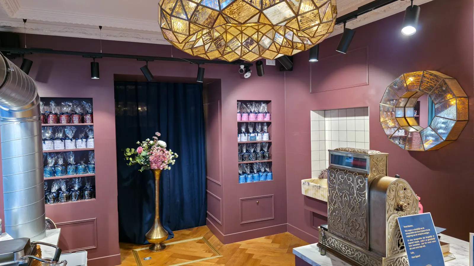 The interior of Hans Egstorf in Amsterdam, with dusty-pink walls, alcove shelves of ribbon-tied tins arranged by colour, a faceted mirror and an antique brass National till