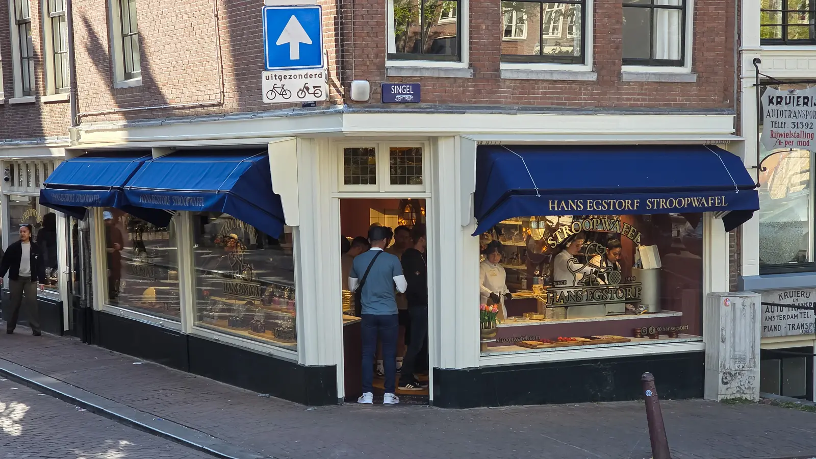 The Hans Egstorf stroopwafel shop on the corner of Singel in Amsterdam, with navy awnings, gold lettering and people at the window