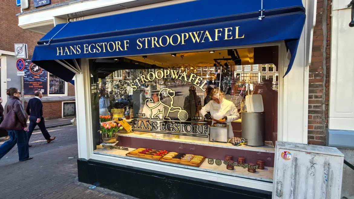 The window of Hans Egstorf in Amsterdam, with the gold lion emblem, the date 1898 and a baker working behind the glass under a blue awning