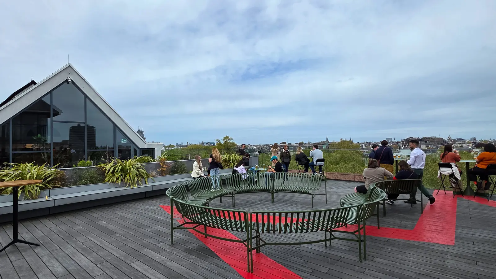 The rooftop terrace at the Heineken Experience in Amsterdam, with green ring benches, a red painted path and the city skyline beyond under cloud