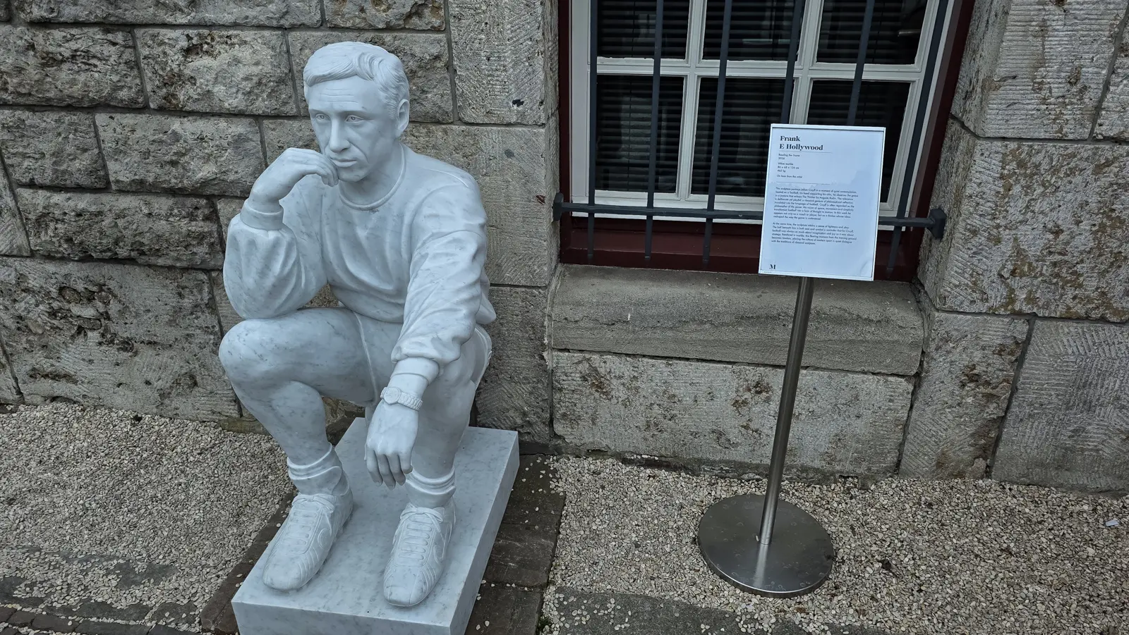 Reading the Game by Frank E Hollywood, a white marble sculpture of Johan Cruyff seated on a football, in the garden at the Moco Museum