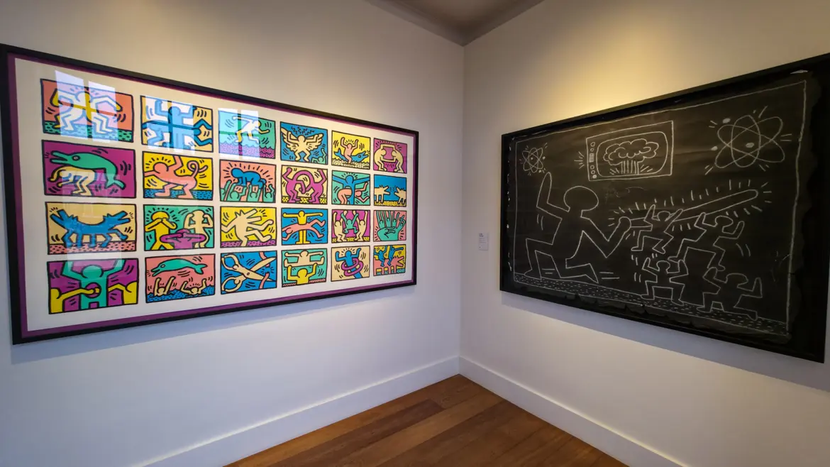 A corner at the Moco Museum, Amsterdam, with a bright Keith Haring screenprint on one wall and a black chalk subway drawing on the other