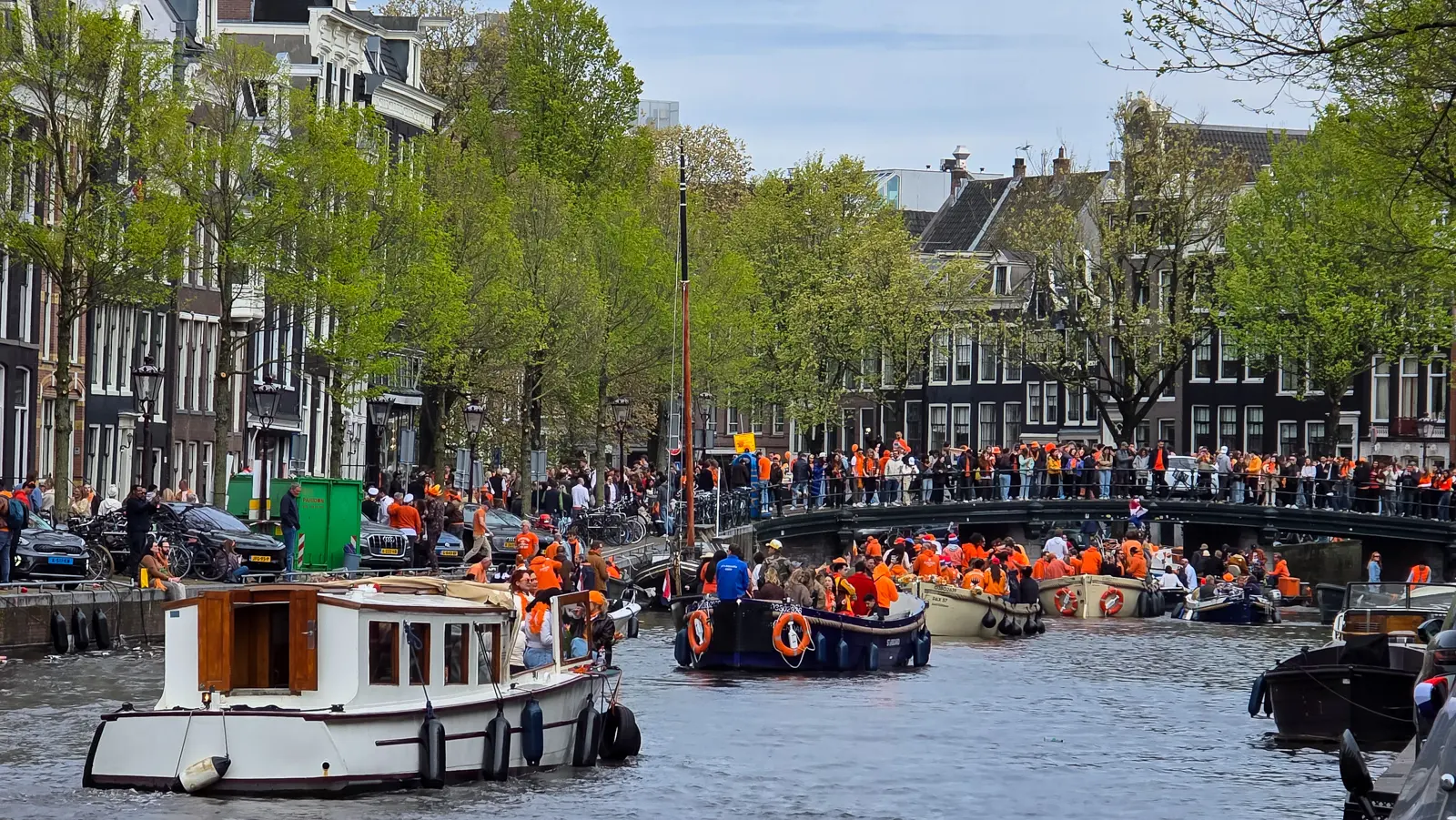 Boats packed with people in orange on an Amsterdam canal on King’s Day, with crowds lining the bridge behind