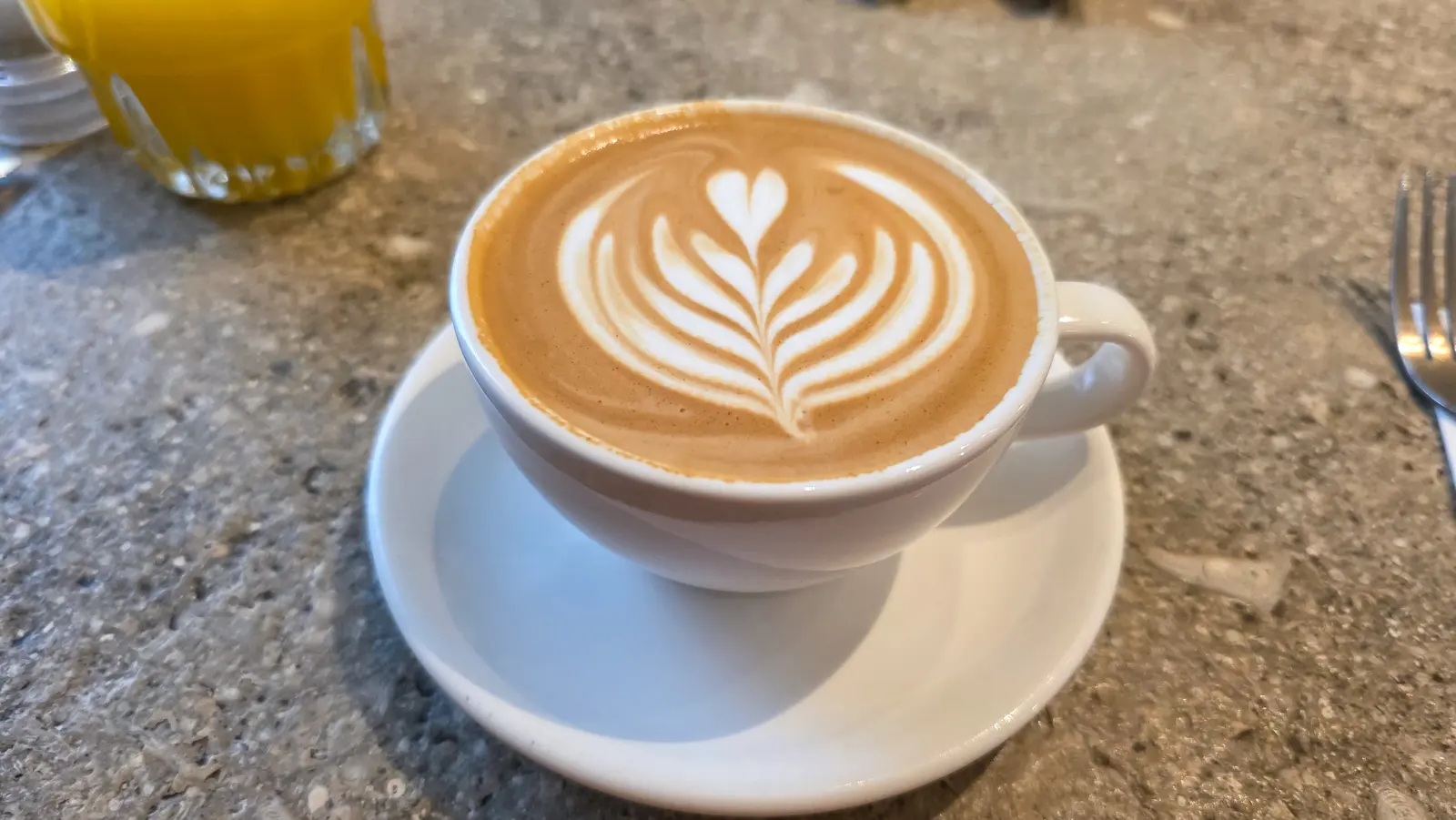 Cappuccino with rosetta latte art in a white cup and saucer at Locals specialty coffee, De Pijp, Amsterdam
