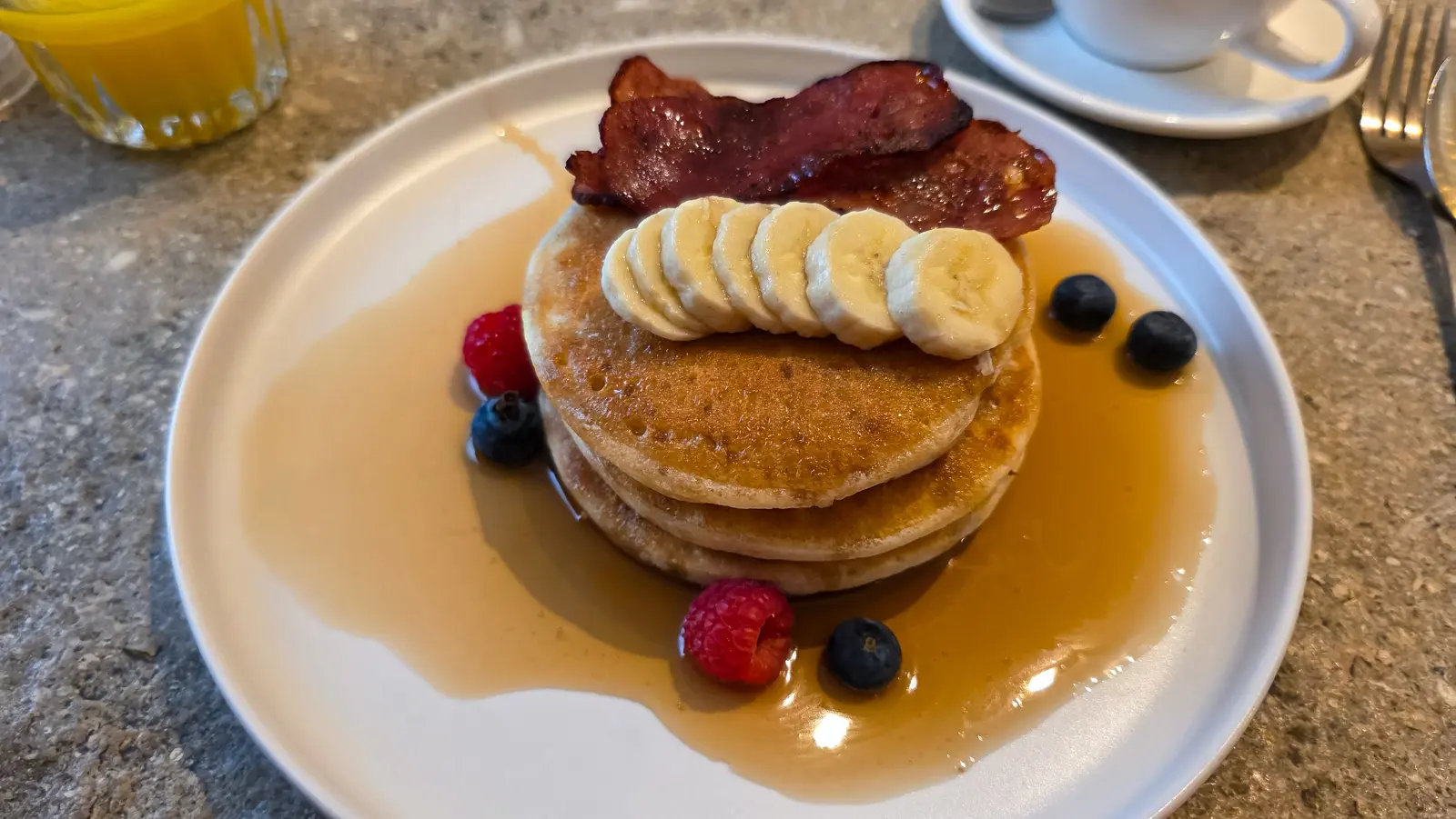 Triple stacked American-style pancakes at Locals Amsterdam with banana, berries, maple syrup and turkey bacon on top