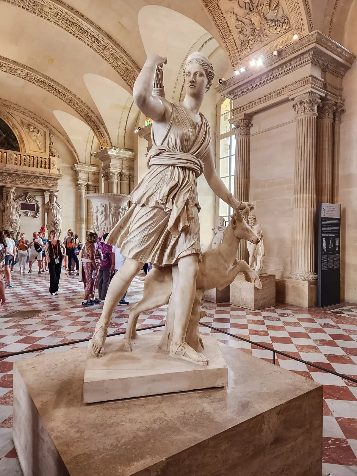 The Diana of Versailles at the Louvre, striding forward in pleated marble drapery with a deer at her side and one arm raised behind