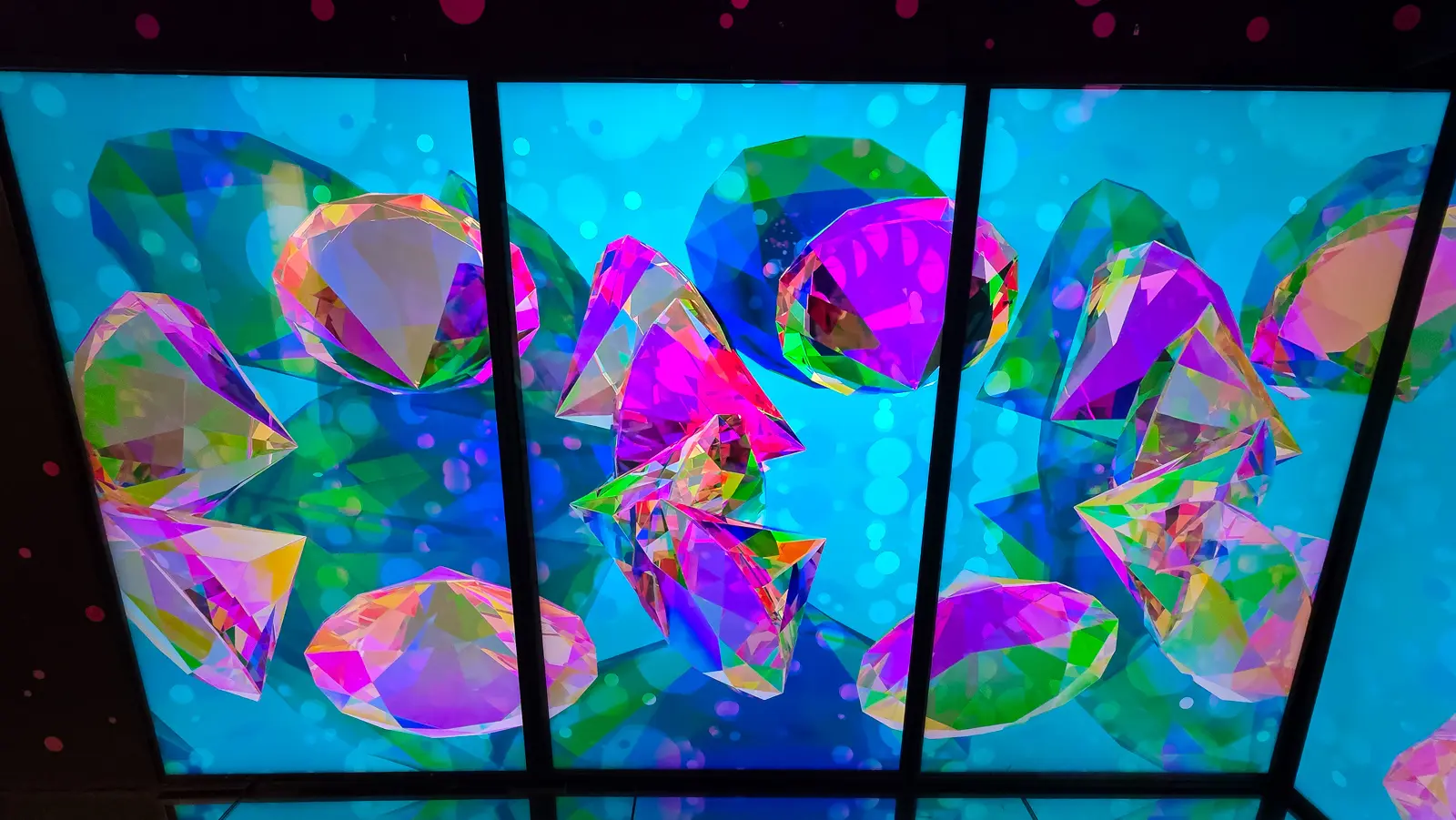 Lit panels of large faceted digital gemstones in green, pink and violet on cyan at Moco Museum Amsterdam, the approach to Diamond Matrix
