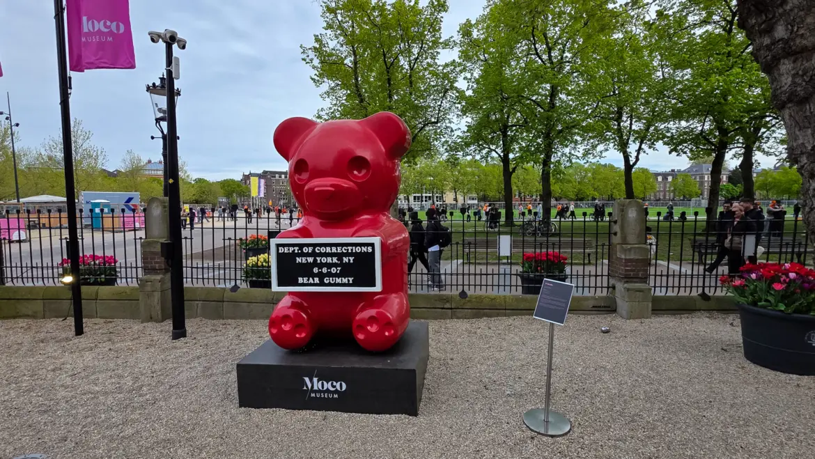 WhIsBe’s Vandal Gummy at the Moco Museum, a large red gummy bear holding a Department of Corrections mugshot board, on a Moco plinth in the forecourt