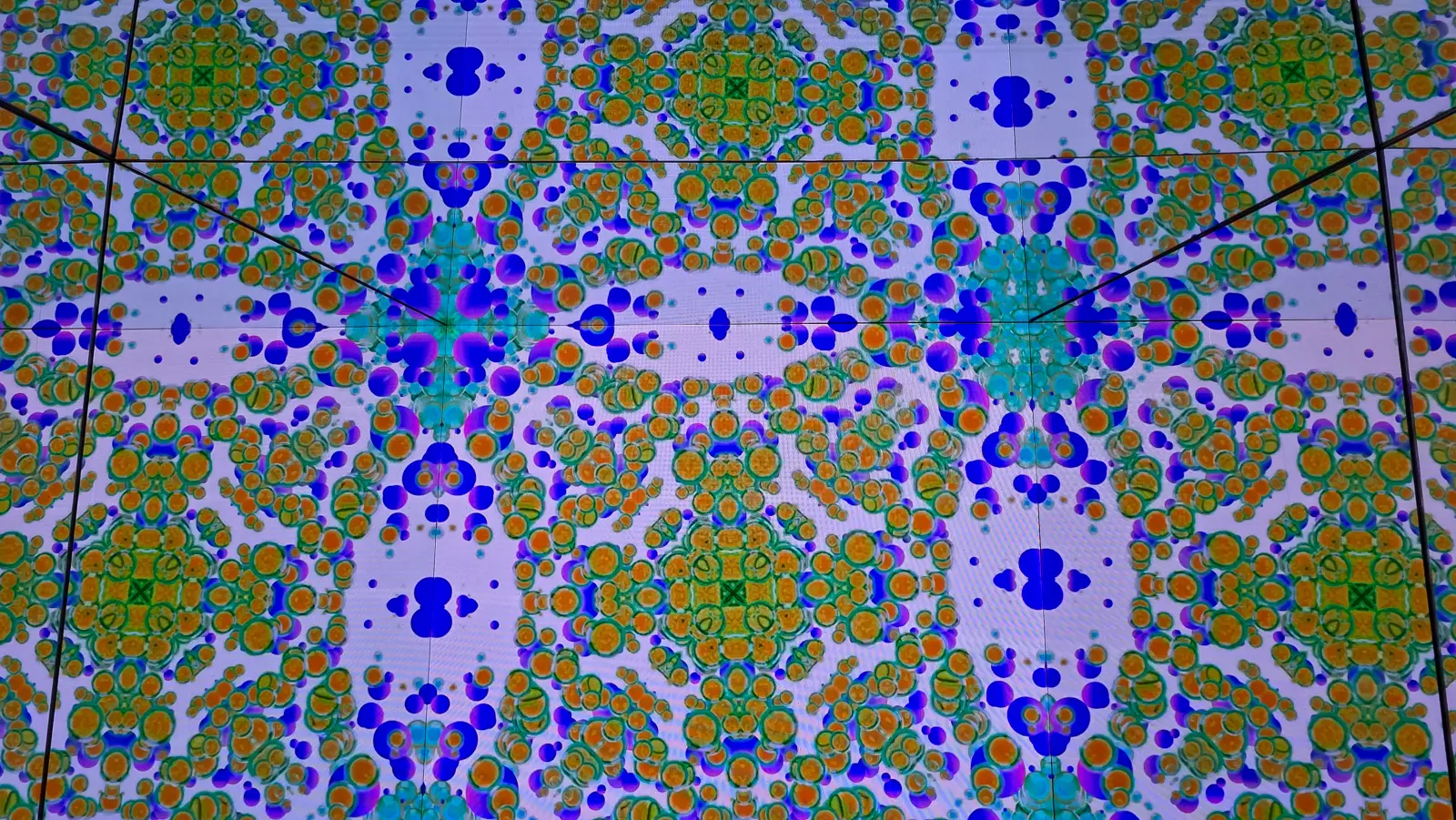 Kaleidoscope at Moco Museum, a mirrored room showing symmetrical orange, green and blue patterns on white