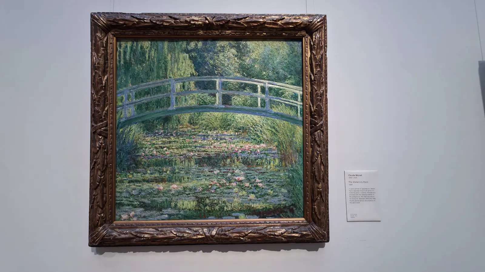 Monet’s The Water-Lily Pond, 1899, in its carved gilt frame on the wall at the National Gallery, London, beside its wall label