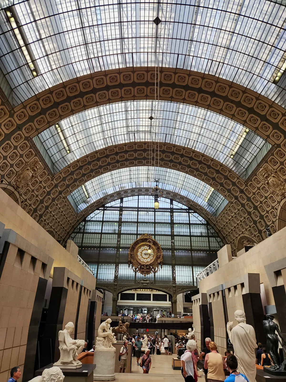 The Musée d’Orsay’s barrel-vaulted hall seen from floor level, with sculptures along both sides and the great gilded clock at the far end