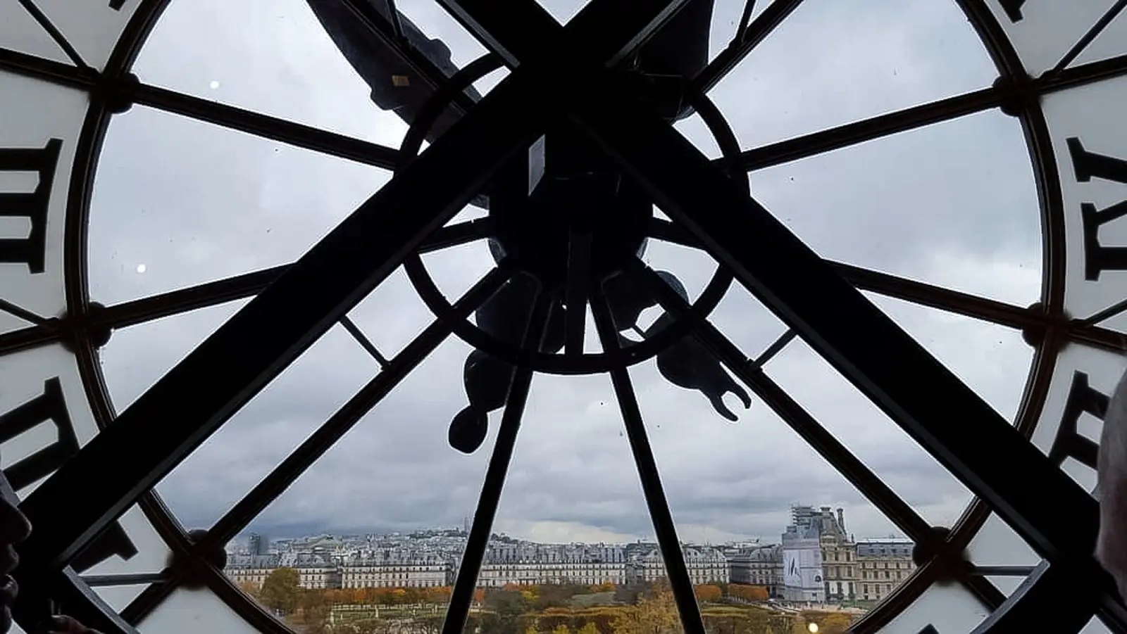 The view out through the glass face of the Musée d’Orsay’s clock, with the ironwork in silhouette and Paris rooftops beyond