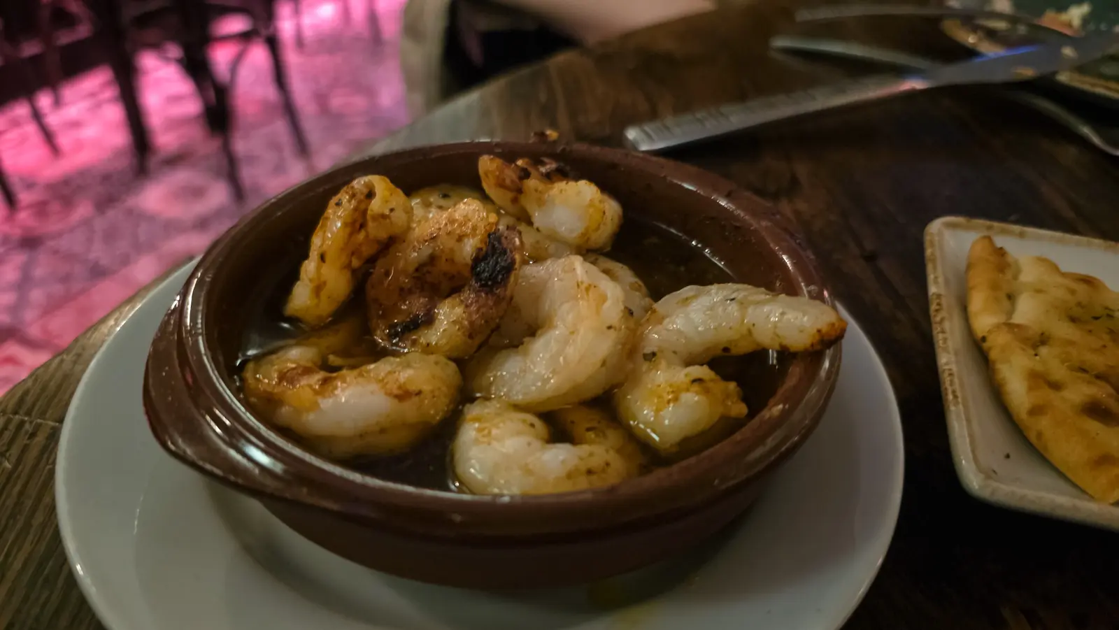 Large prawns in a terracotta dish with oil and herbs at Oresti’s Taverna, a piece of pita alongside