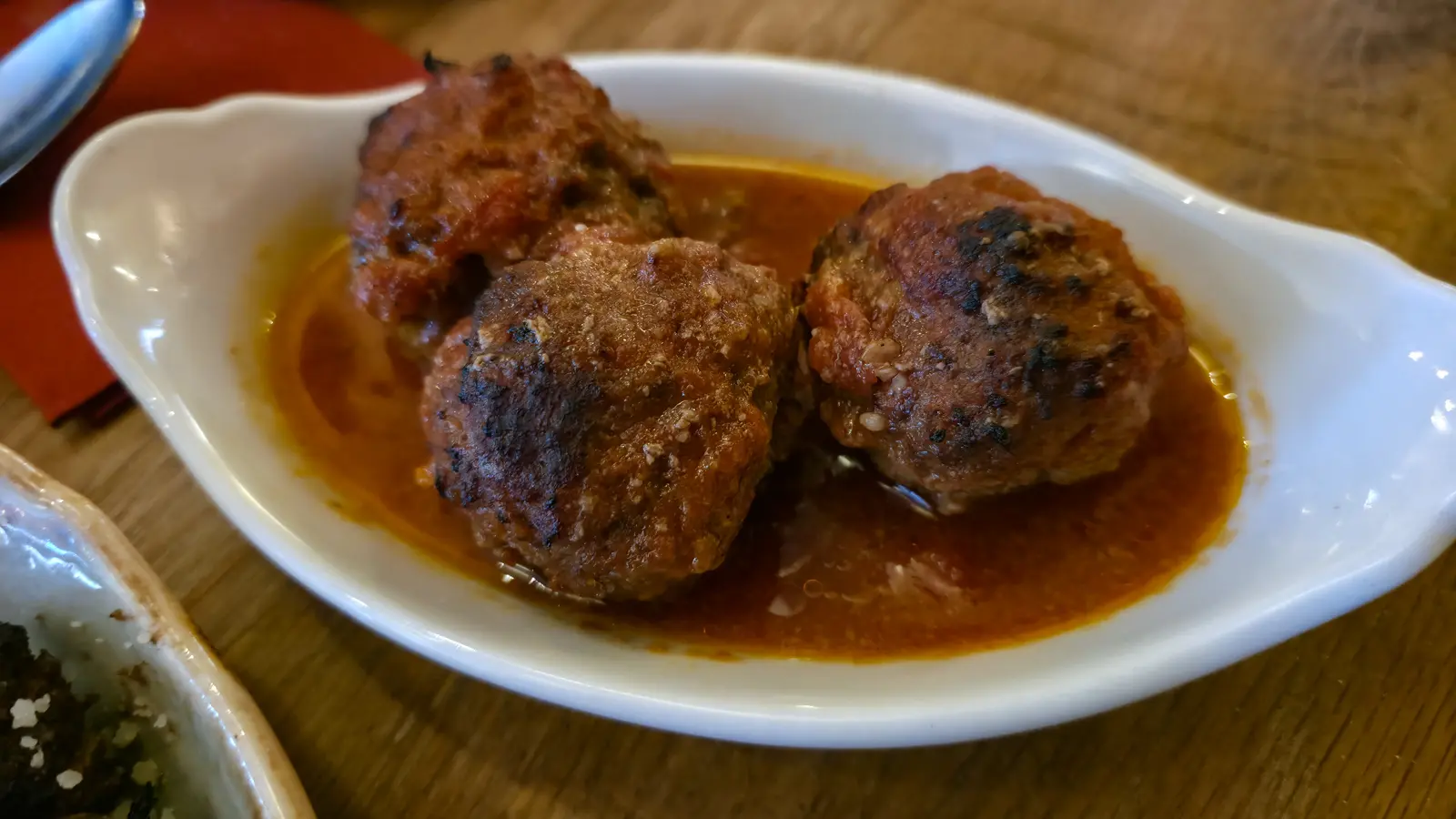 Three soutzoukakia meatballs in tomato sauce in a white dish at Oresti’s Taverna, Amsterdam