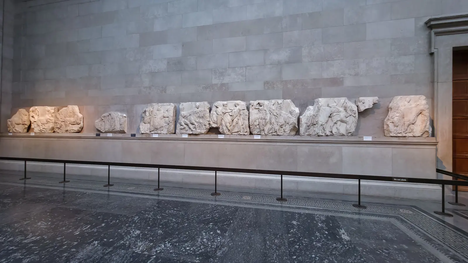 A row of the Parthenon Marbles, carved marble panels from the ancient temple in Athens, lining a gallery wall at the British Museum