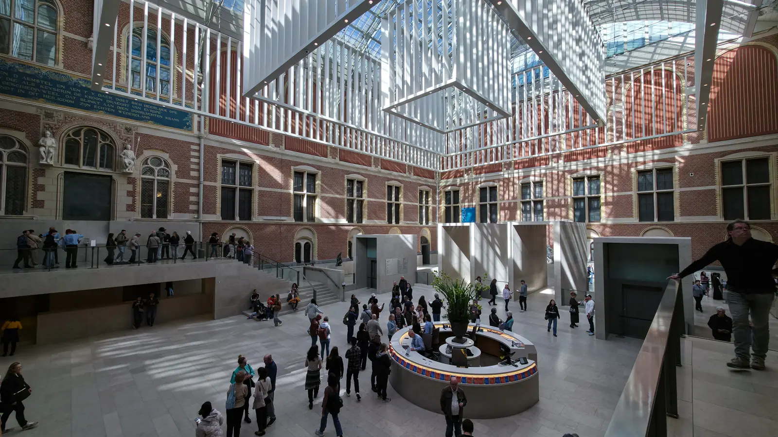 The Rijksmuseum atrium, with brick courtyard facades rising to a glazed roof and visitors gathered around the circular information desk