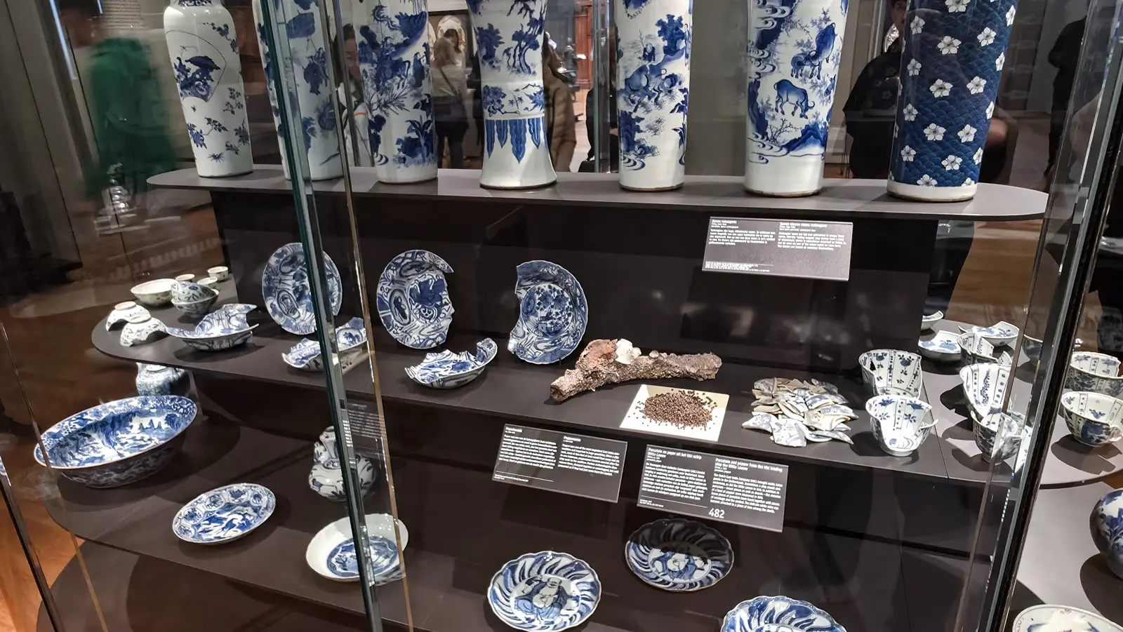 A display case of blue-and-white porcelain at the Rijksmuseum, with vases above and plates, bowls and shards laid out below
