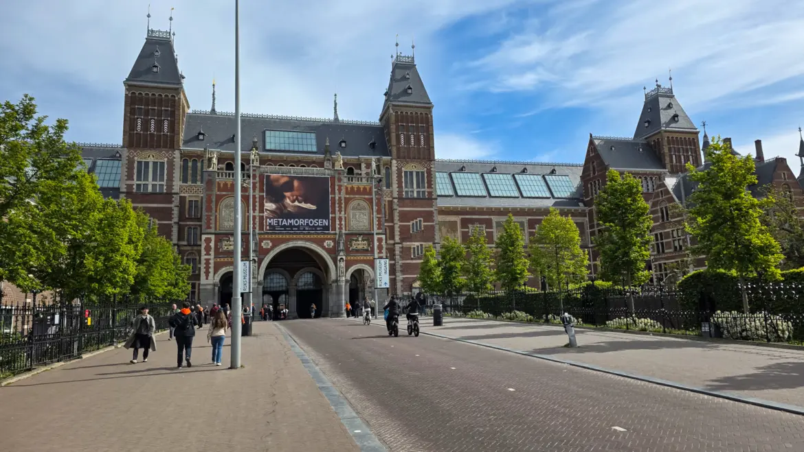 The Rijksmuseum’s brick and stone facade with its twin towers and central archway, seen from the approach road in Amsterdam