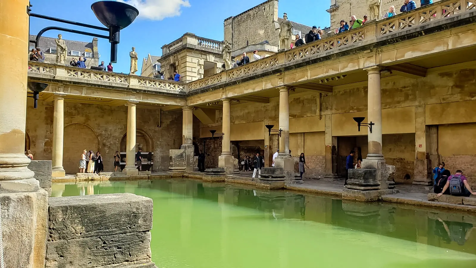The Great Bath at the Roman Baths from poolside, green water ringed by columns and a statue-topped terrace, a day trip from London