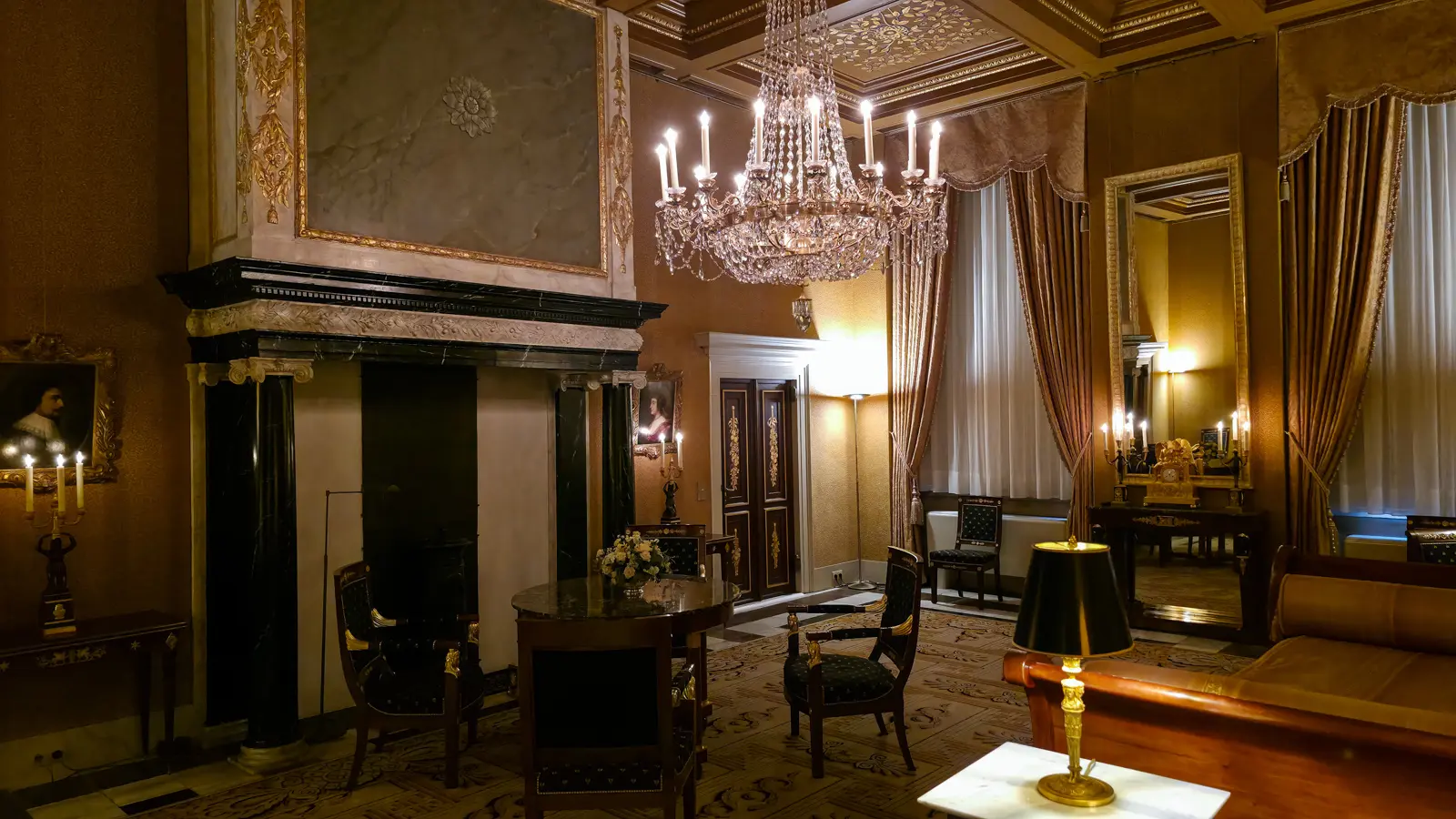 A gold-toned room in the Royal Palace Amsterdam with a crystal chandelier, black marble chimneypiece and Empire furniture