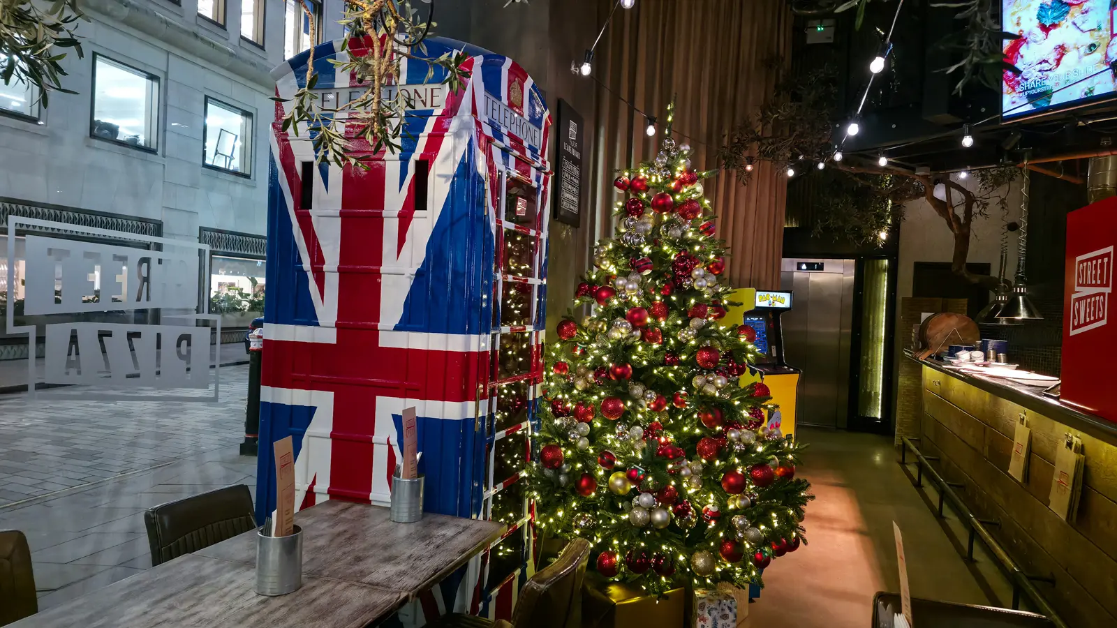 Inside Street Pizza at One New Change, with its Union Jack phone box, arcade machine and a lit Christmas tree, near St Paul’s