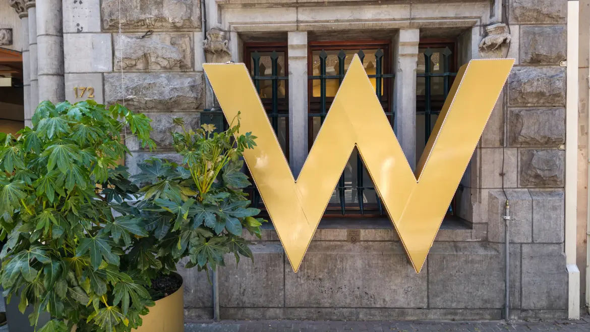 Gold W sculpture and green foliage against the stone facade of the W Amsterdam hotel’s Bank building at Spuistraat 172