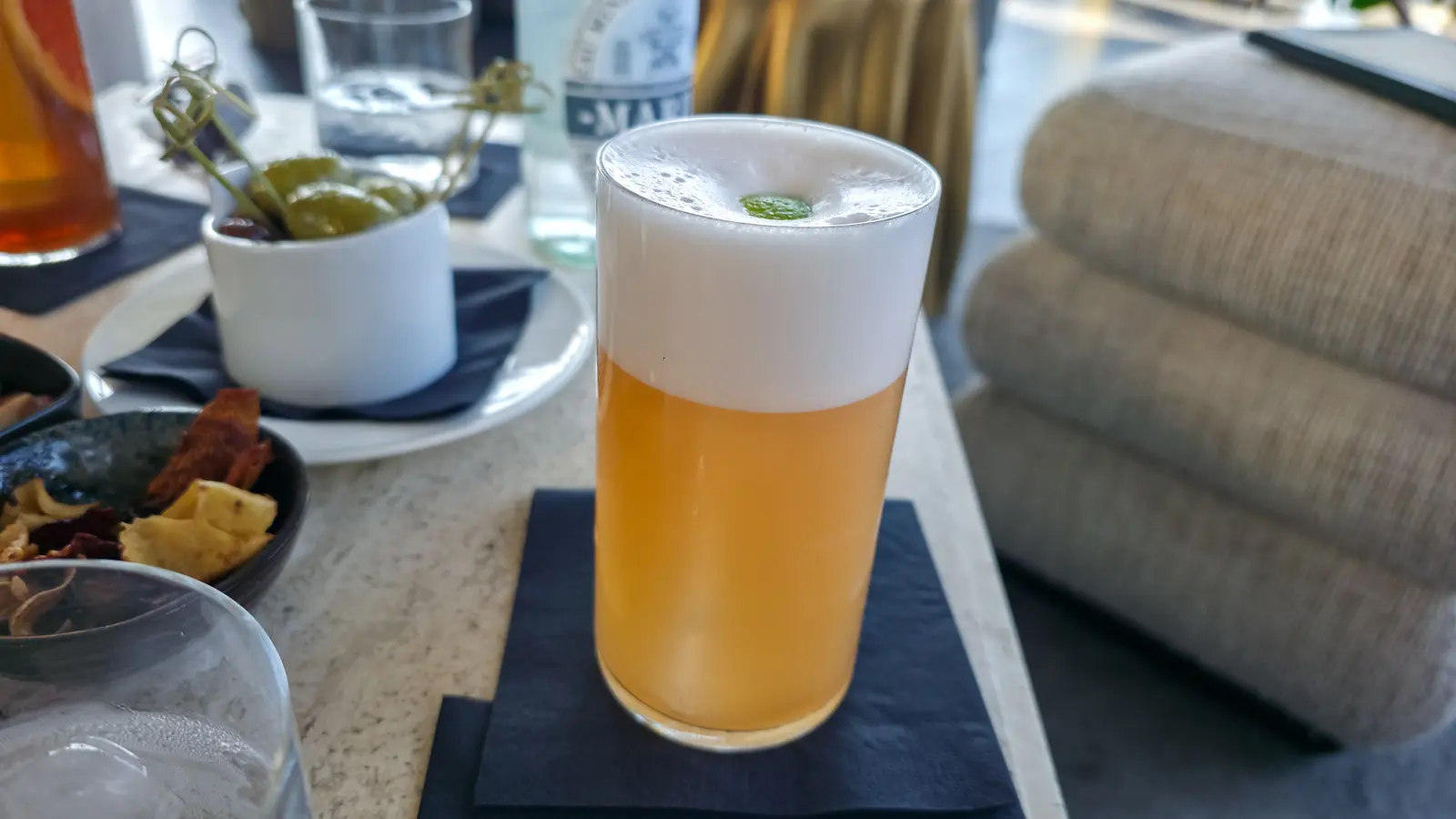 The Bittersweet Symphony at the W Lounge, W Amsterdam, a pale cocktail under a deep foam with a small green garnish set into the top