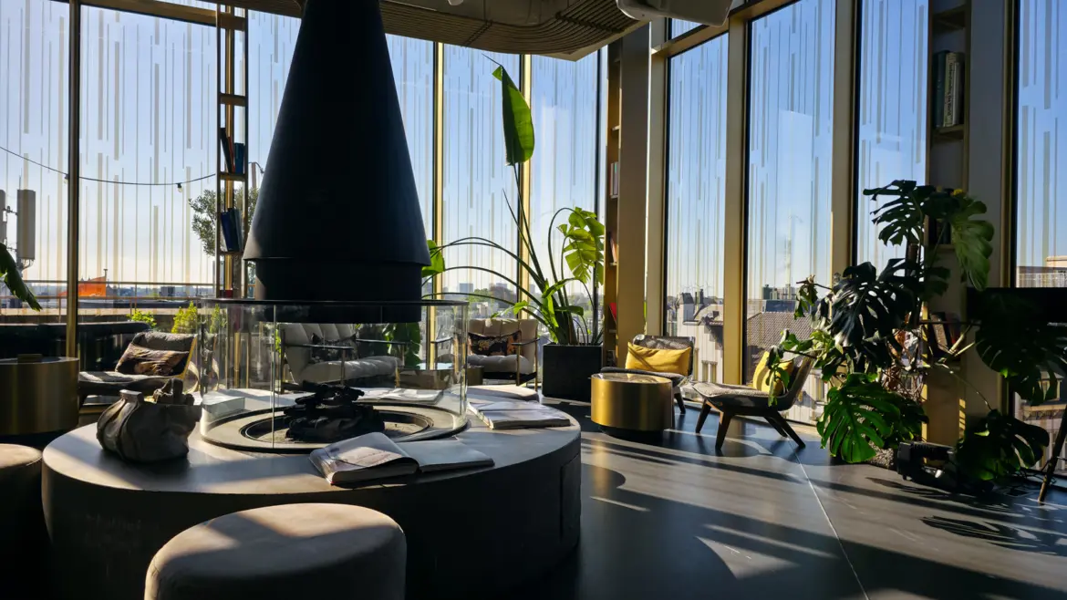 Black conical fireplace with a curved glass screen in the W Lounge at the W Amsterdam, with plants, books and glass walls