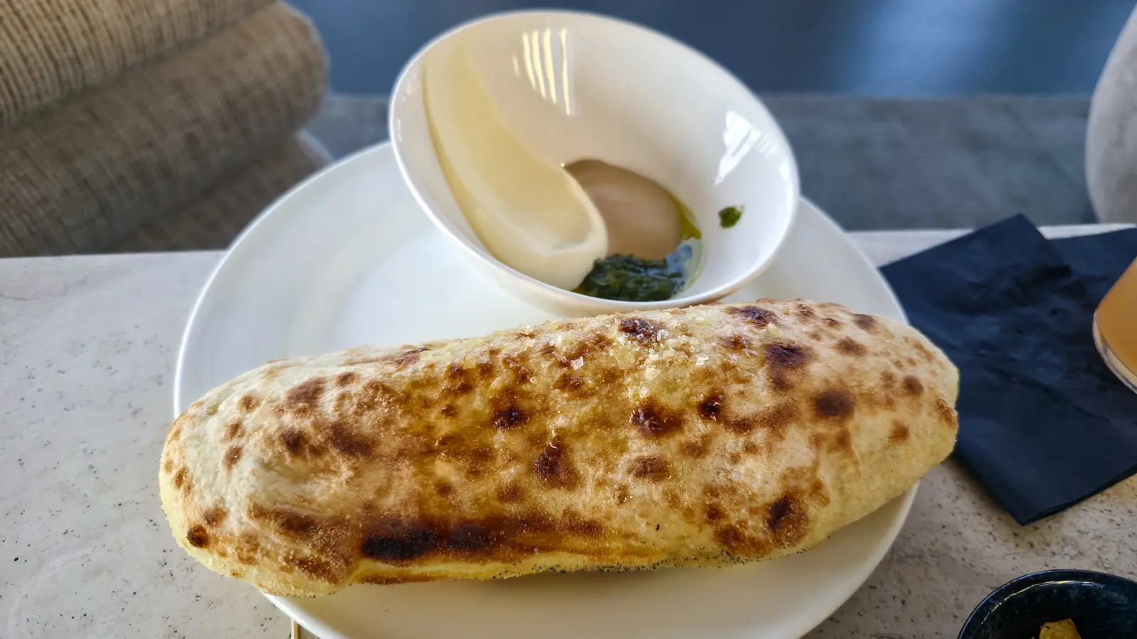 A whole homemade focaccia on a white plate with a bowl of dips, on a stone table at the W Lounge in Amsterdam