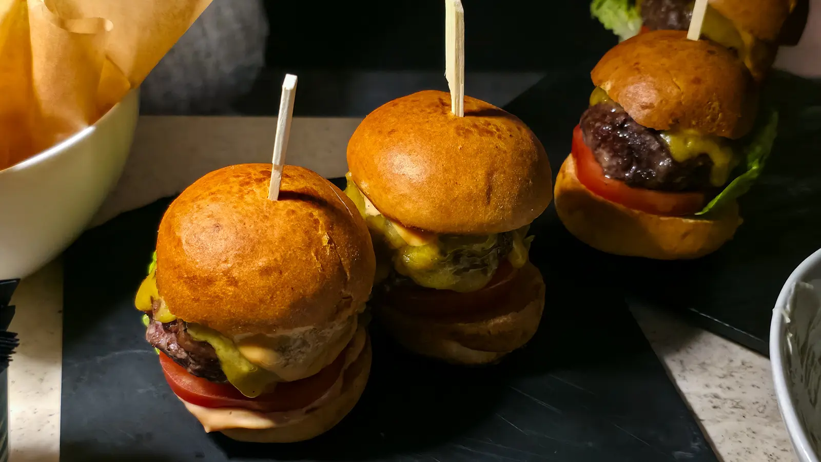 Mini cheeseburgers with tomato, cheese and sauce, held together with wooden skewers, on a slate board at the W Lounge
