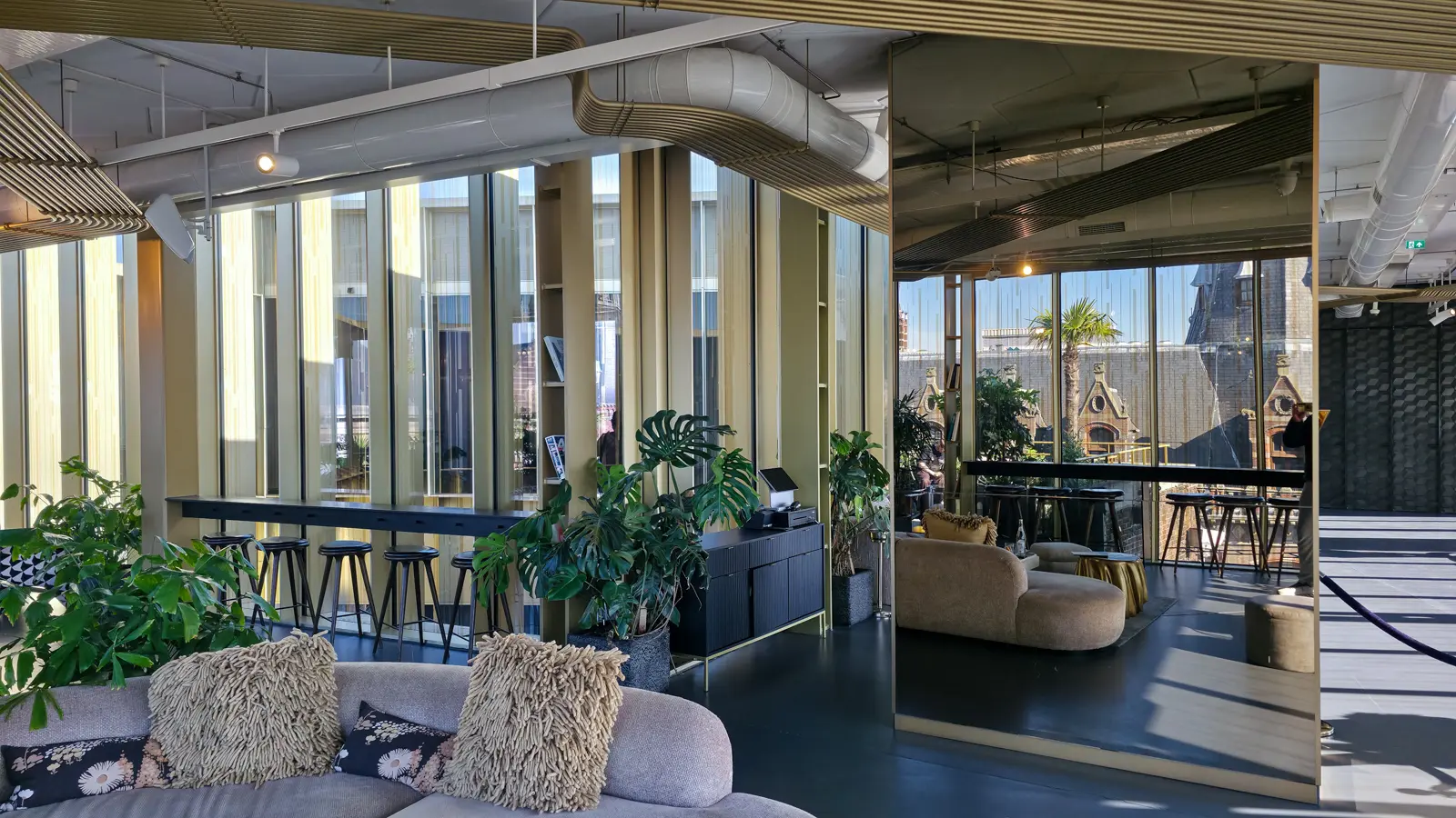 Bar seating and a mirrored column in the W Lounge at the W Amsterdam, with the terrace and a palm visible through the glass