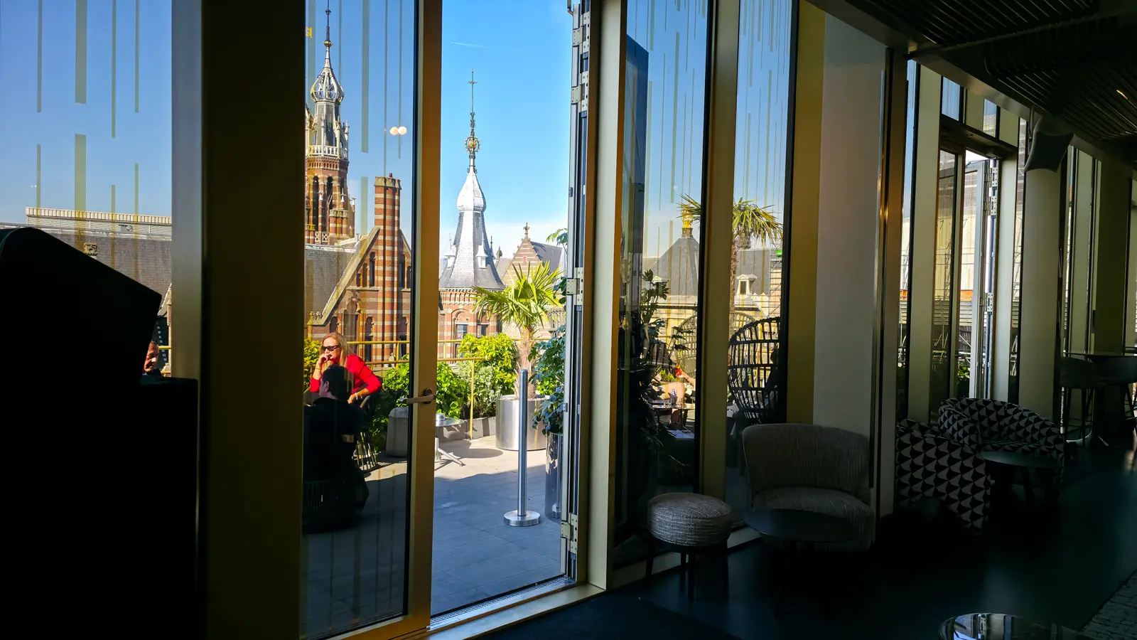 Folding glass doors open onto the rooftop terrace at the W Amsterdam, with brick turrets and spires beyond in afternoon sun