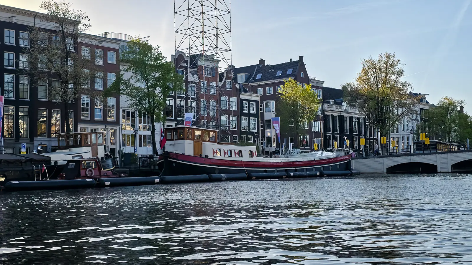 A red-and-black converted barge with a wooden wheelhouse and red-and-white painted shutters, moored on the Amstel in Amsterdam