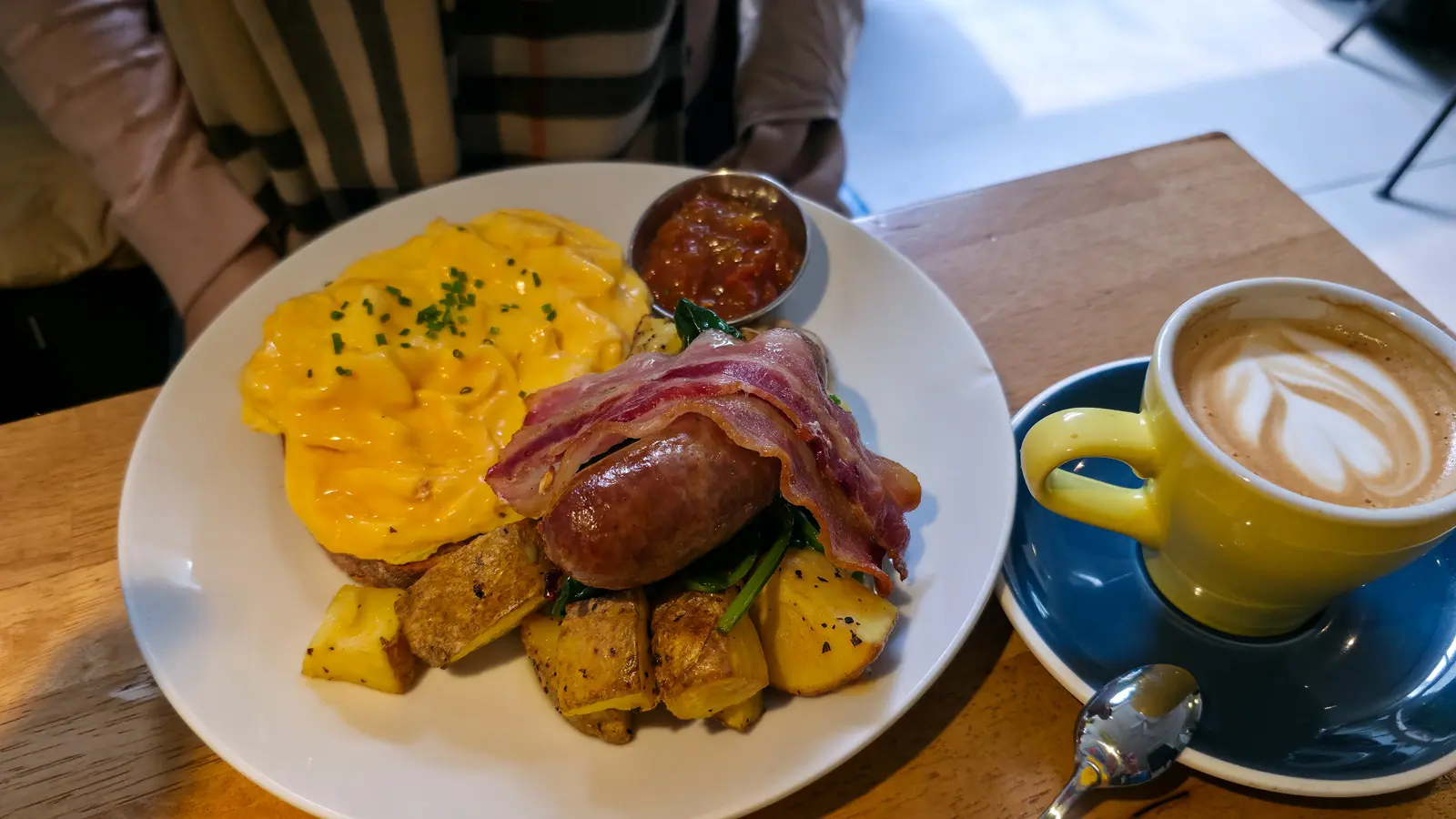 The Kiwi Brekkie at Bakers & Roasters: soft scrambled eggs with chives, a sausage, bacon, skin-on breakfast potatoes, spinach and a pot of tomato relish, with a flat white