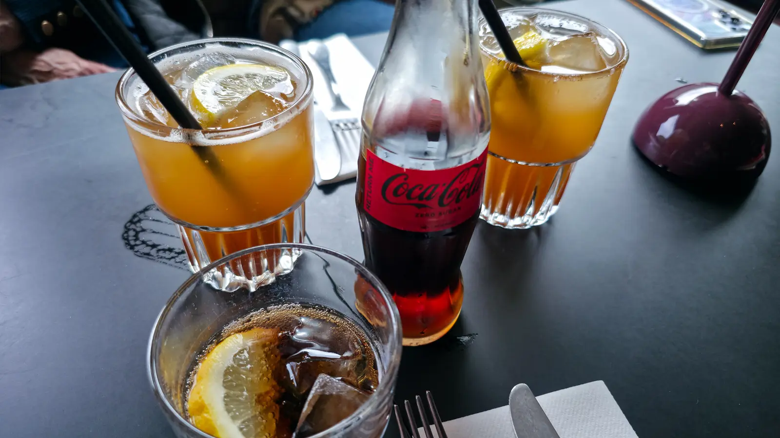 Two glasses of Van Gogh Juice with lemon and ice on a dark table at Bistro Vincent, Van Gogh Museum, Amsterdam, beside a bottle of cola