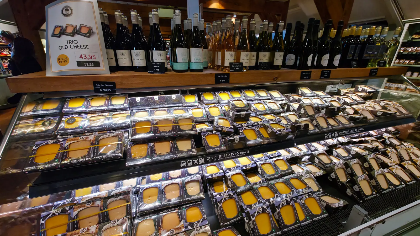 Case of extra old cheeses with a Trio Old Cheese offer sign and a shelf of wine bottles above, Catharina Hoeve, Zaanse Schans
