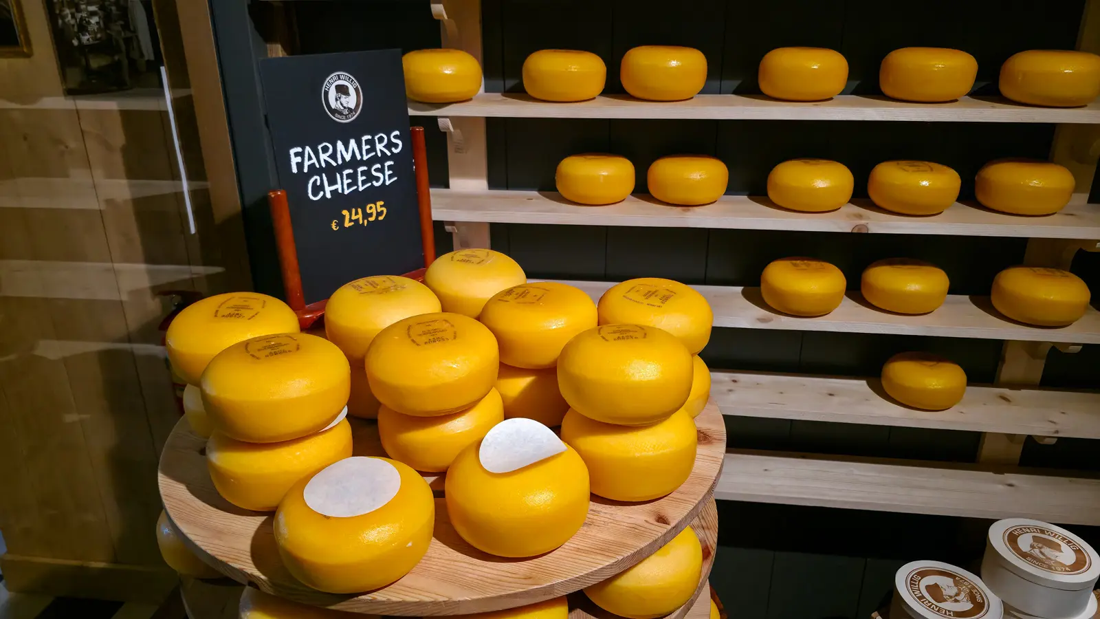 Stacked wheels of Farmers Cheese at 24.95 euros beside racks of yellow cheese, Catharina Hoeve shop, Zaanse Schans