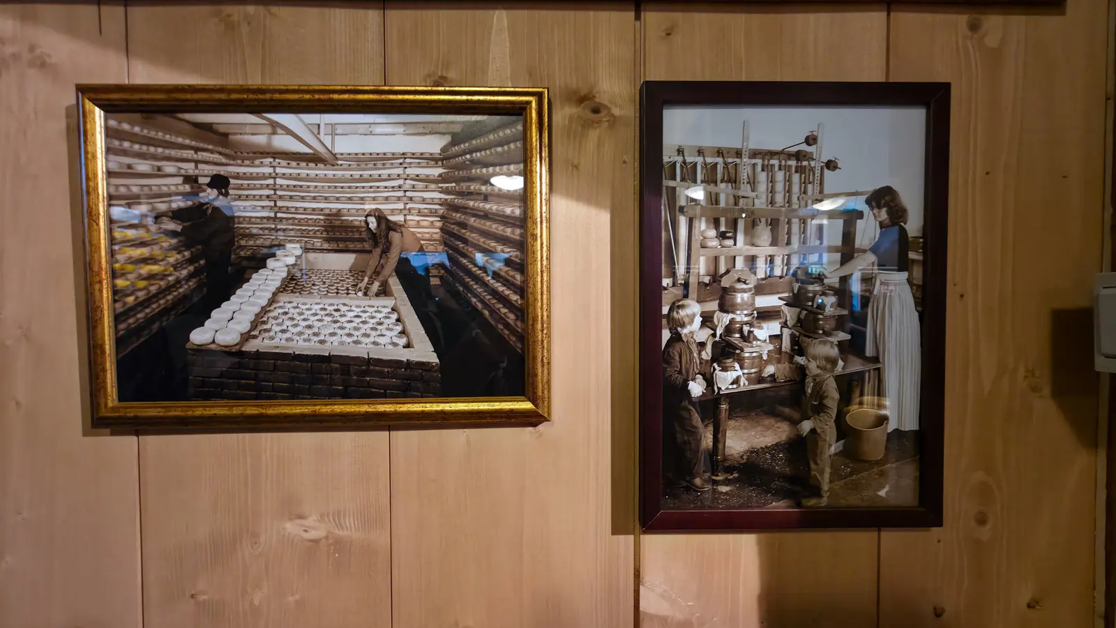 Two framed historic photographs on pale wood panelling, one of a cheese loft and one of a woman and two children at cheese moulds