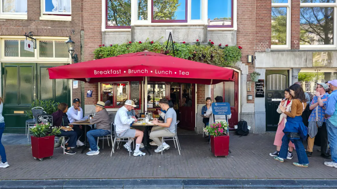 Greenwoods at Singel 103 in Amsterdam, a red Breakfast Brunch Lunch Tea umbrella over a busy terrace with diners and a queue on the right