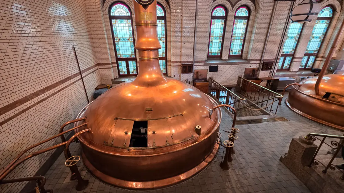 Copper brewing kettle under stained glass windows and glazed brick in the historic brew room, Heineken Experience, Amsterdam