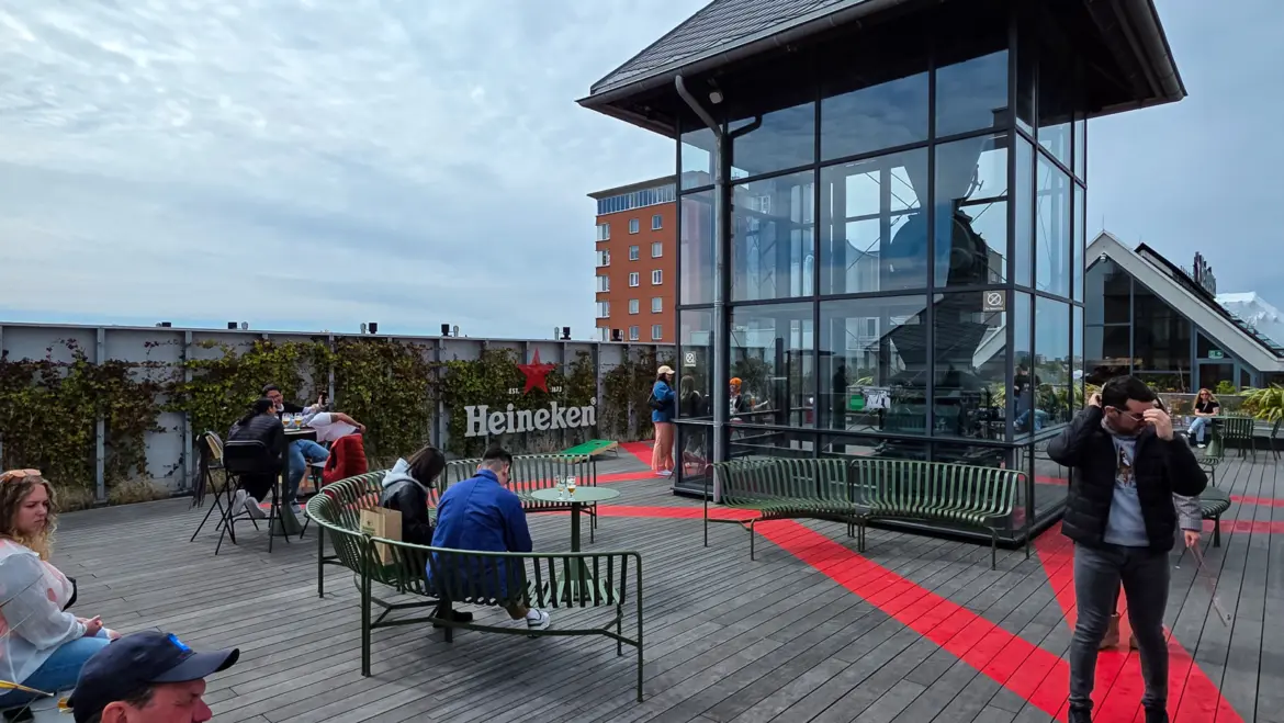 Rooftop terrace at the Heineken Experience, Amsterdam, with timber decking, green benches and the Heineken sign on an ivy wall