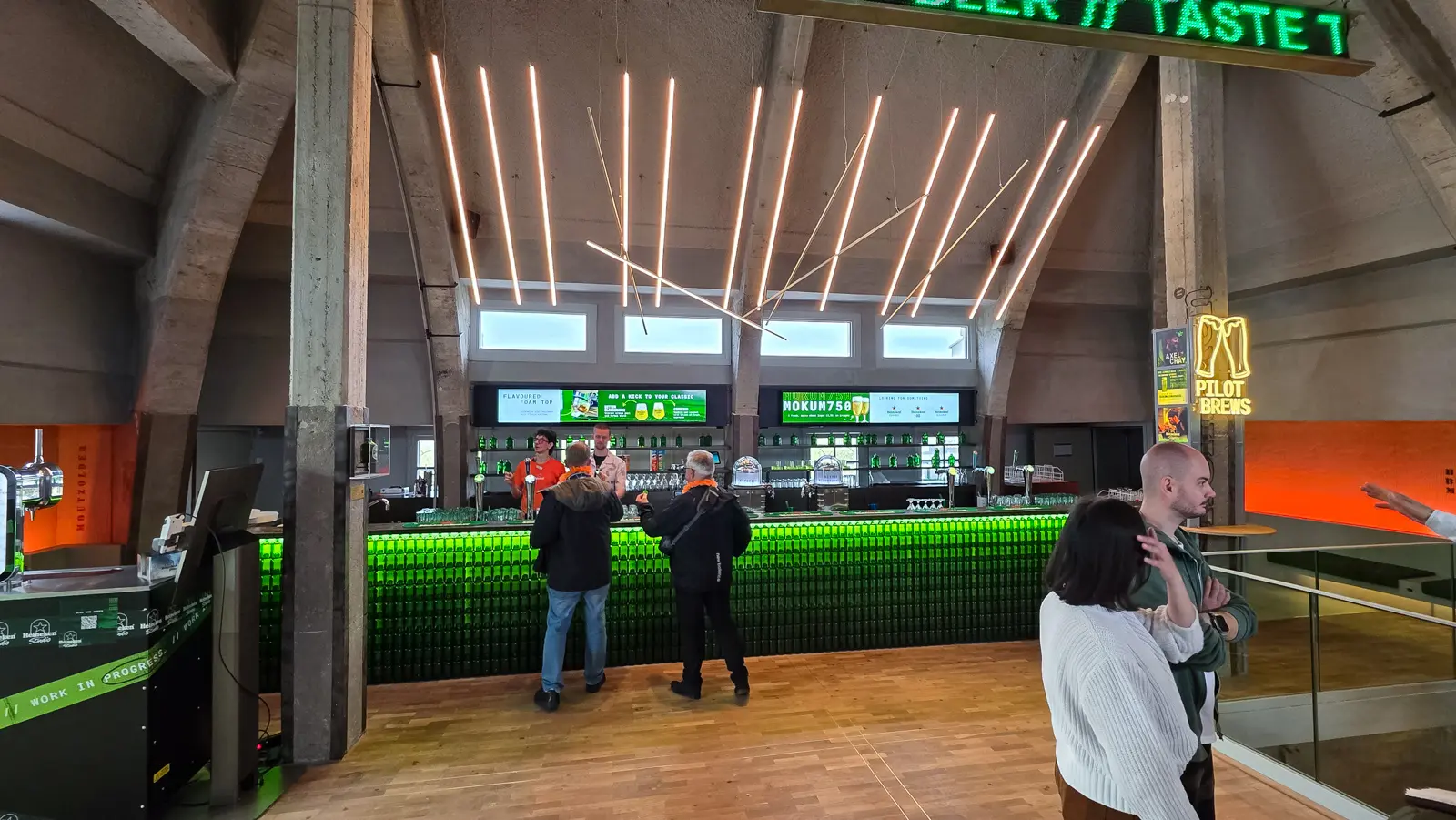 Top-floor bar at the Heineken Experience, Amsterdam, its front built from stacked green bottles, under a ceiling of suspended light tubes